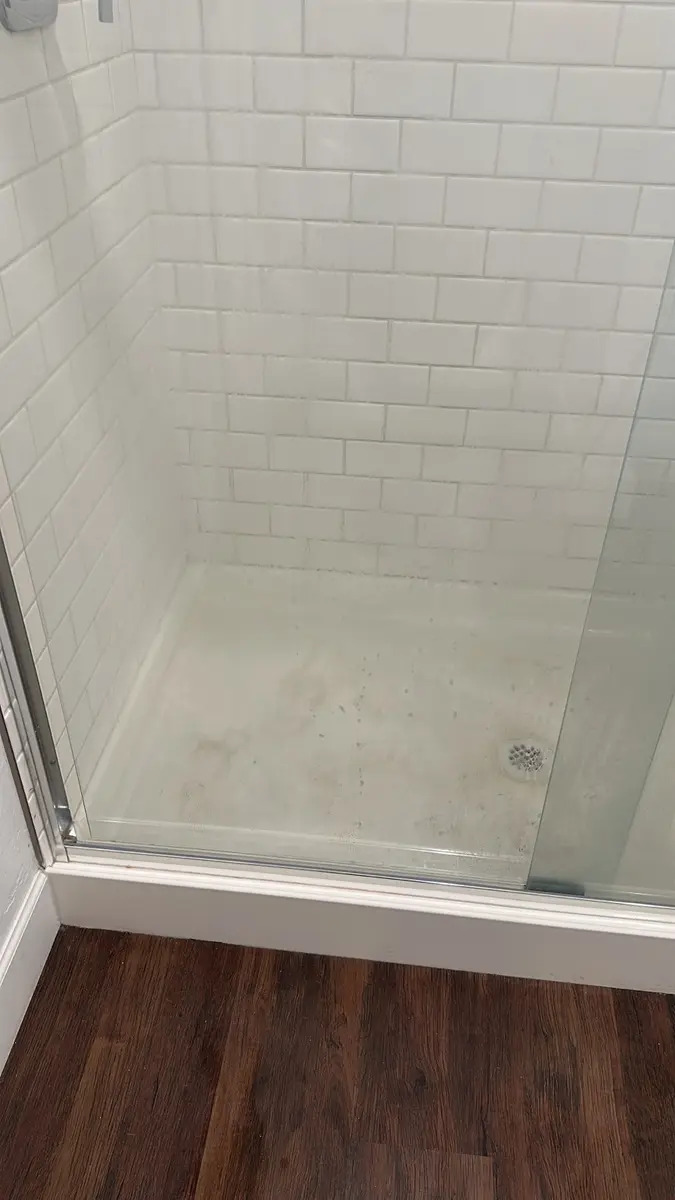 Stained shower pan and glass before a Handy Girlz deep cleaning